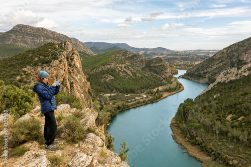 Woman taking pictures in countryside, on top of mountain overlooking river, mountains in background