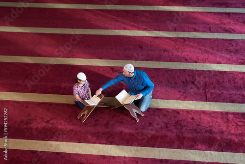 Muslim Man teaching his little son to pray to Allah and teachinh him reading Koran at mosque during ramadan.