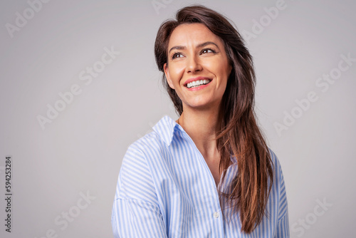 Studio portrait of attractive woman wearing shirt and laughing while sitting at isolated grey background. © sepy