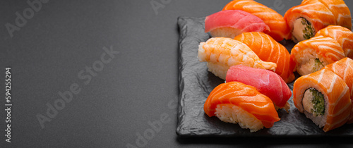 Set of traditional Japanese sushi and rolls angle view with soy sauce and wasabi on dark black rustic slate. Sushi with salmon, tuna and shrimp, space for text