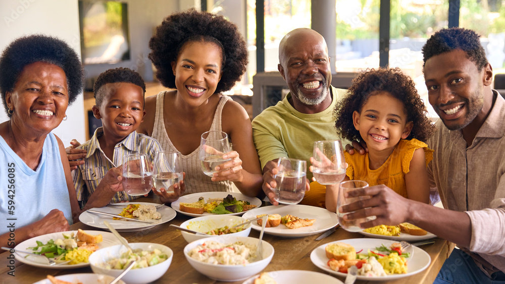 Multi-Generation Family Around Table Doing Cheers With Water Before Serving Food For Meal At Home Multi-Generation Family Around Table Doing Cheers With Water Before Serving Food For Meal At Home