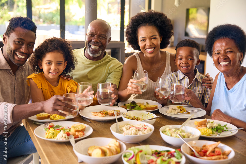 Multi-Generation Family Around Table Doing Cheers With Water Before Serving Food For Meal At Home Multi-Generation Family Around Table Doing Cheers With Water Before Serving Food For Meal At Home
