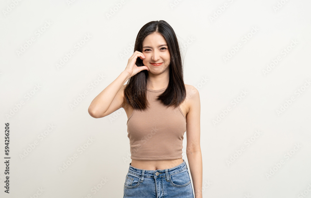 Pretty Young beautiful Asian woman standing and smiling showing mini heart sign on cheek isolated on white background. Lovely female wearing brown shirt feeling surprised and happy. Pretty Young beautiful Asian woman standing and smiling showing mini heart sign on cheek isolated on white background. Lovely female wearing brown shirt feeling surprised and happy.