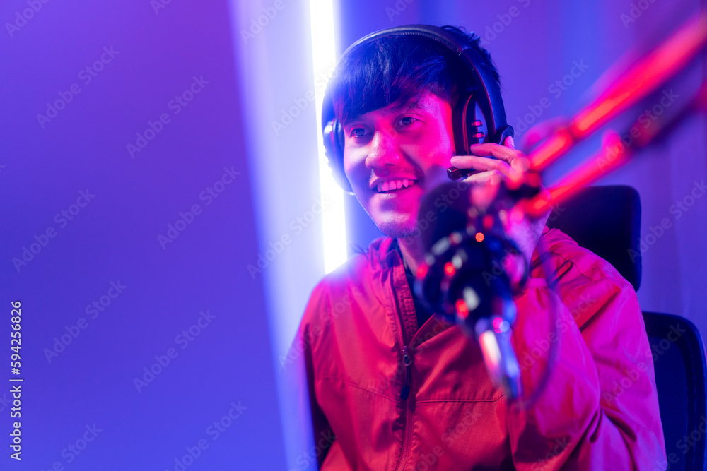 Professional gamer casting podcast walkthrough review. Young asian man sitting on chair with computer pc and microphone. Happy male Streamer wearing headphone playing game online in room neon light Professional gamer casting podcast walkthrough review. Young asian man sitting on chair with computer pc and microphone. Happy male Streamer wearing headphone playing game online in room neon light