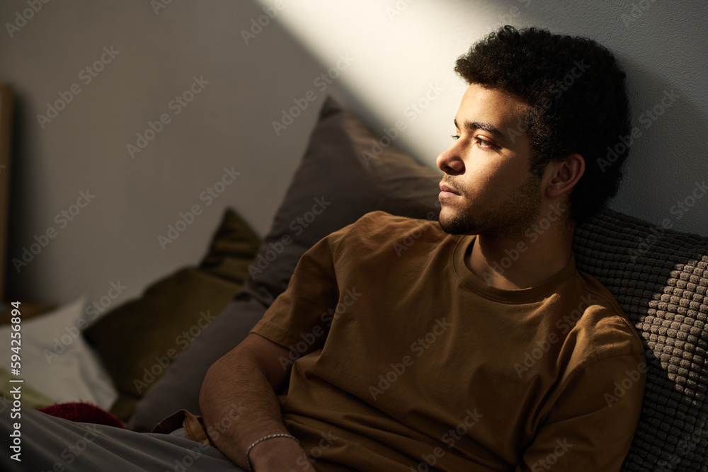 Sad teenage boy worried about his problems sitting alone on bed in his room - obrazy, fototapety, plakaty 