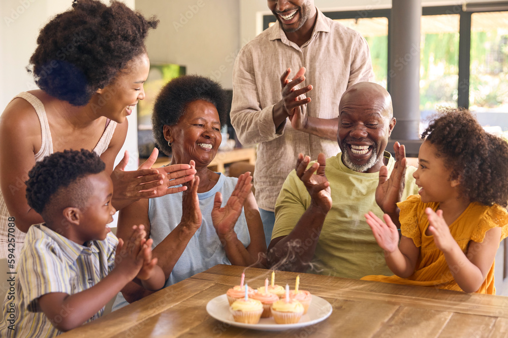 Multi-Generation Family Celebrate Grandmother's Birthday With Cake And Candles Around Table At Home 