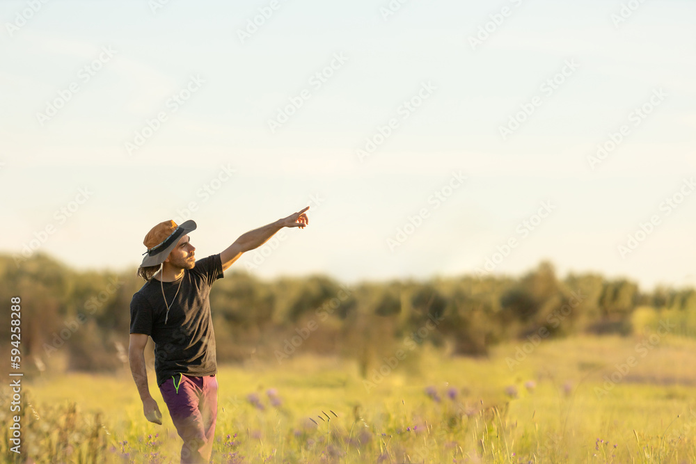 Man pointing to sky, in middle of meadow, with trees in background, at sunset, space to write Man pointing to sky, in middle of meadow, with trees in background, at sunset, space to write