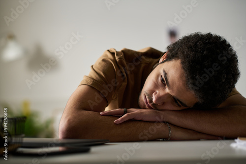 Young depressed man sitting at table with sad expression staying alone in the room