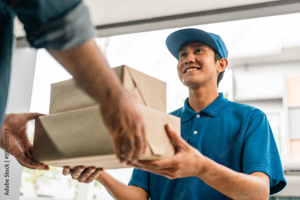 Asian delivery man with parcel in hand of blue uniform sending parcel to customer front of the house from shopping online with good service. Courier man send a package to destination. Asian delivery man with parcel in hand of blue uniform sending parcel to customer front of the house from shopping online with good service. Courier man send a package to destination.