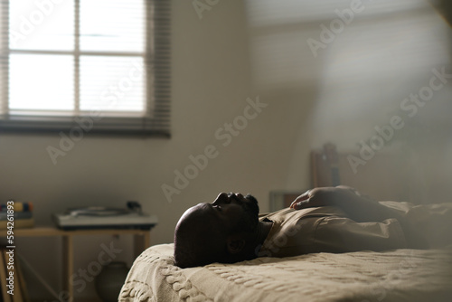 African American man in melancholy lying on bed alone in his bedroom