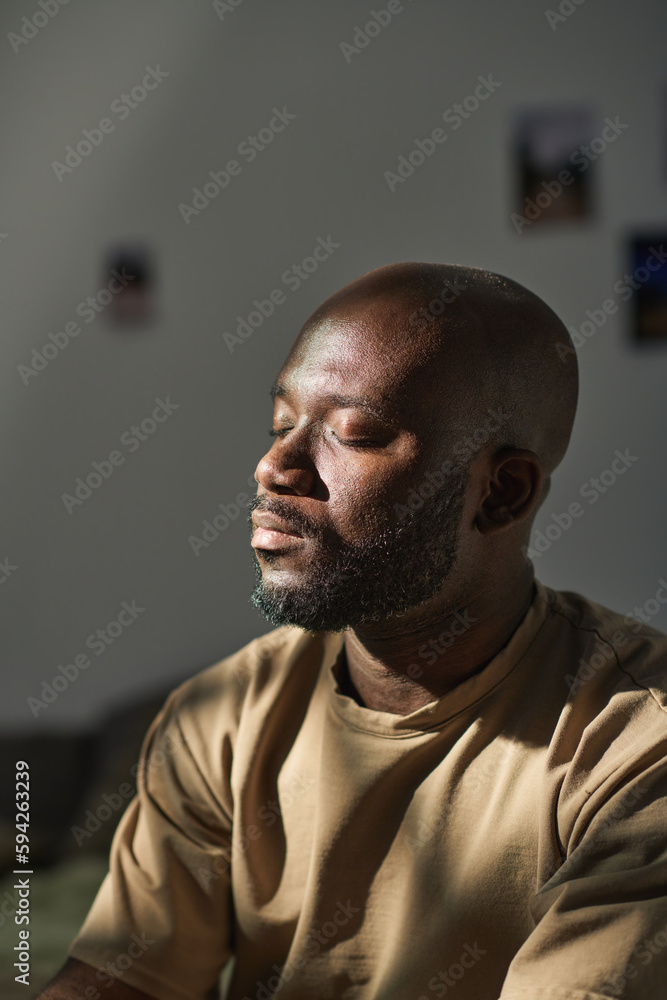 Vertical image of African American man sitting with his eyes closed and meditating at home Vertical image of African American man sitting with his eyes closed and meditating at home