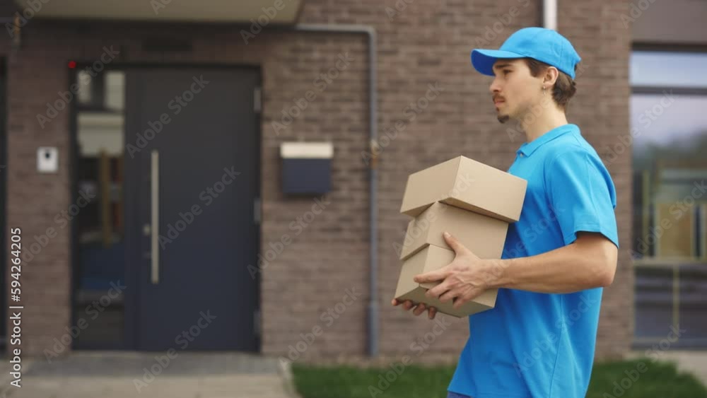 Side View of the Caucasian Male Postman Walking Holding the Paper Boxes. Walking Outside. Male Delivery Wearing Special Uniforms Carrying the Boxes. People and Professions. Delivering Service Side View of the Caucasian Male Postman Walking Holding the Paper Boxes. Walking Outside. Male Delivery Wearing Special Uniforms Carrying the Boxes. People and Professions. Delivering Service