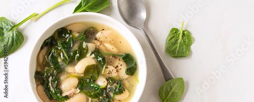 bowl of soup with white beans and spinach on a light table