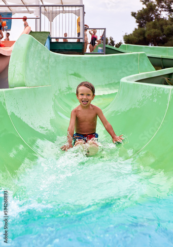 Joyful boy descends from the water slide in the water park, children's attractions in the water park, water slides, children's entertainment on vacation