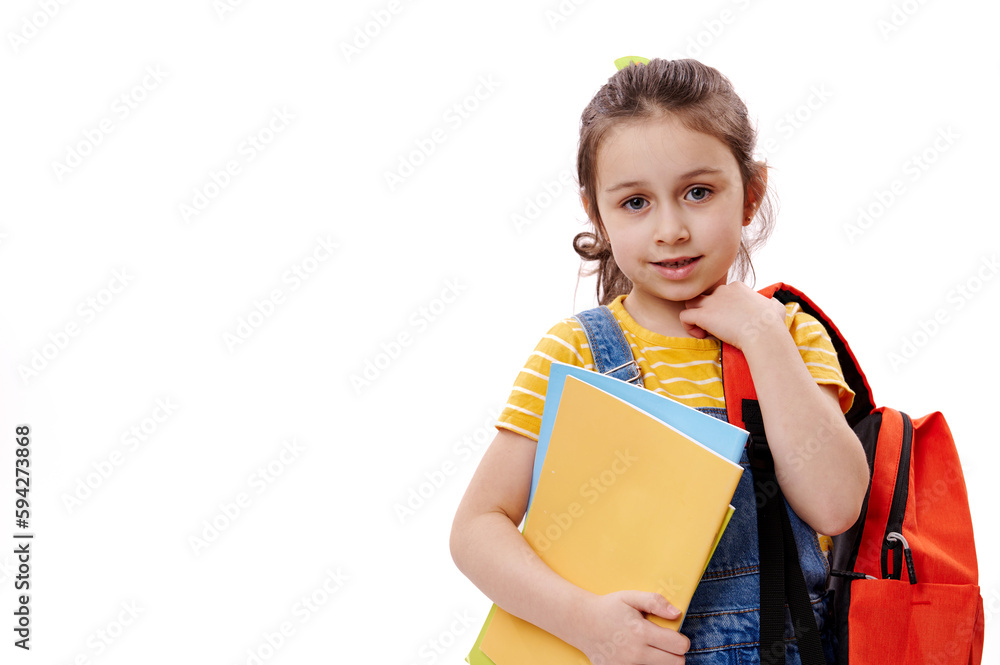 Horizontal portrait of Caucasian smiling excellent best student, first grader schoolgirl, 5-6 years old little girl holding books and looking at camera, isolated on white background. Copy ad space Horizontal portrait of Caucasian smiling excellent best student, first grader schoolgirl, 5-6 years old little girl holding books and looking at camera, isolated on white background. Copy ad space