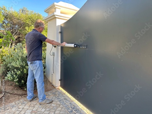 Cuadro en lienzo Man inspecting the hydraulic ram on an electric gate opener