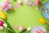 Mother's day dining setup. Top view flat lay of colorful plates, cutlery, beautiful presents, paper hearts and tulips on light green background with copy space for text or greeting message