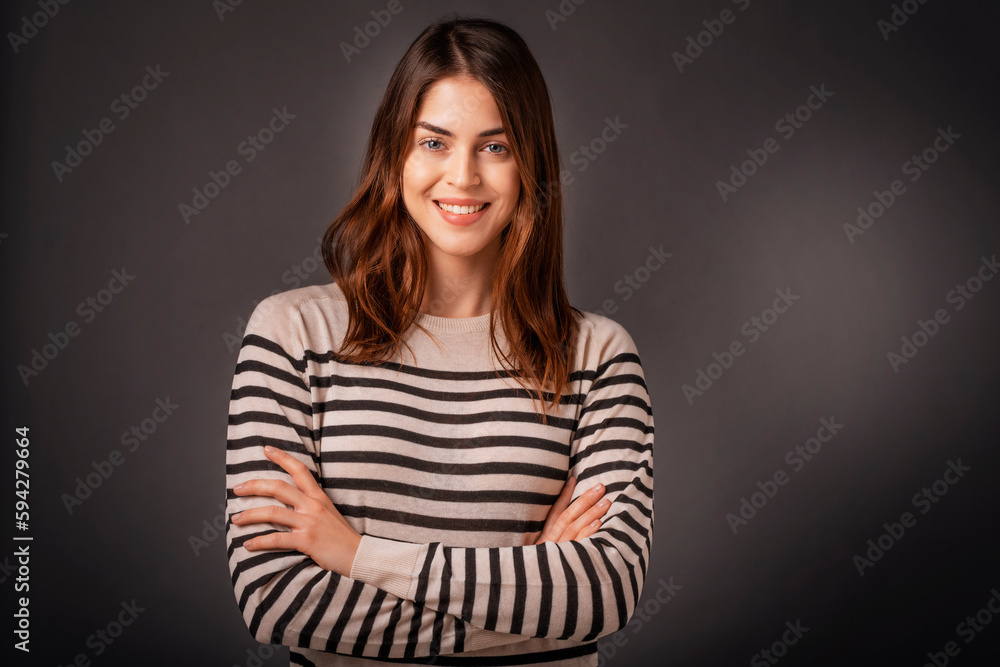 Obraz premium Close-up of confident young woman with folded arms against dark background