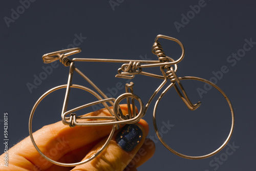 A metal bicycle in a woman's hand against a dark blue-gray sky. Holding a toy mini bike. Cycling in mountains. Round aluminum wheels of a bike. Healthy lifestyle, outdoor leisure and sports concept.
