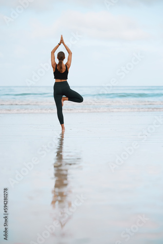 The steadiness in the tree pose helps you calm your mind. Rearview shot of a young woman doing a tree pose while practising yoga at the beach.