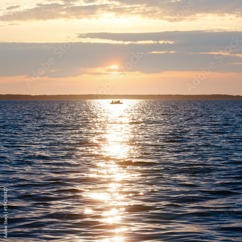 Sun track and fishing boat on lake surface.