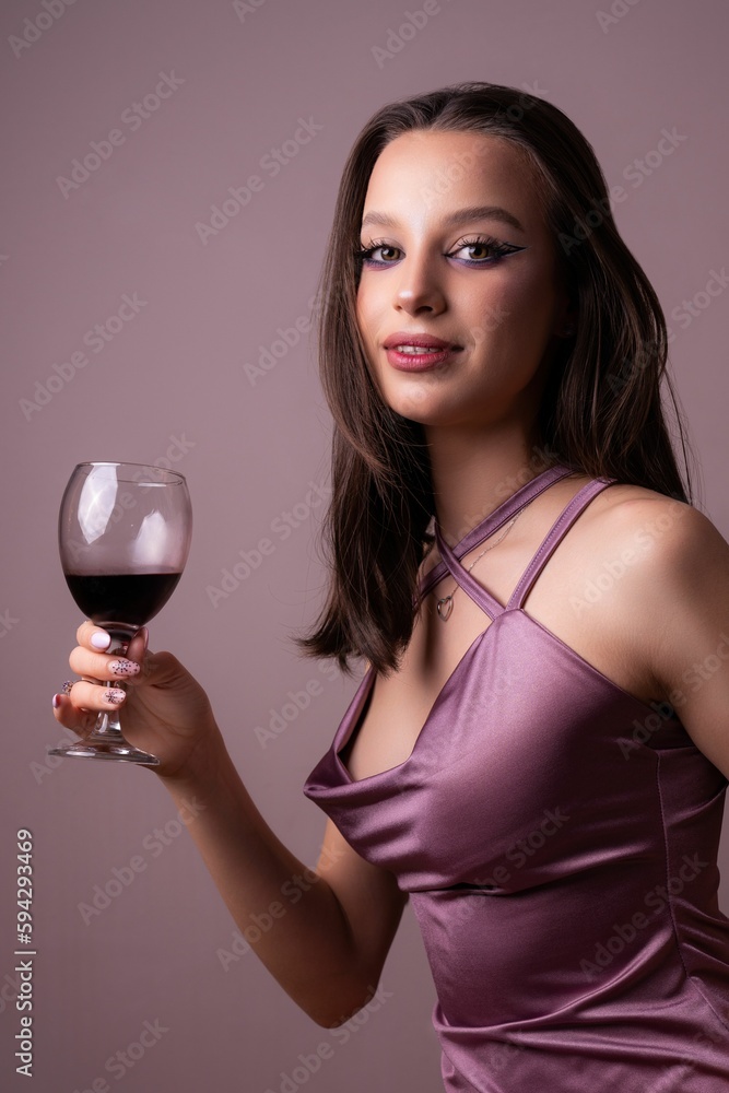 Beautiful Caucasian brunette in sexy purple dress holding red wine glass against purple wall Beautiful Caucasian brunette in sexy purple dress holding red wine glass against purple wall