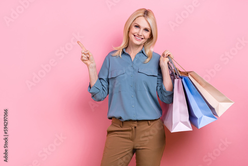 Photo of cheerful good mood optimistic promoter business lady direct finger empty space hold bags shopping promo isolated on pink color background