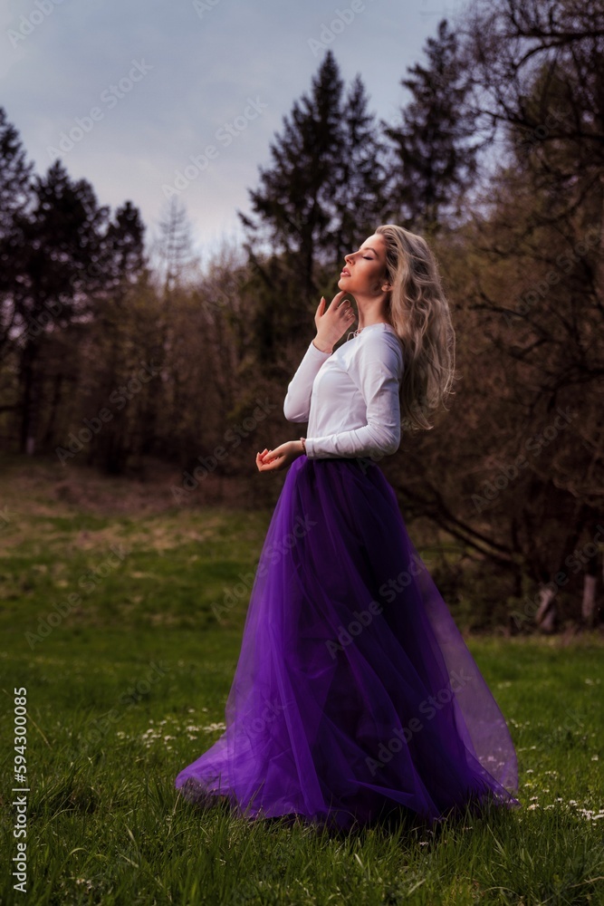 Young female posing in a white shirt and a purple tulle skirt in a park