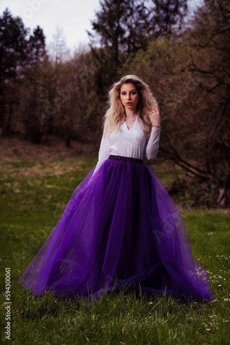 Young female posing in a white shirt and a purple tulle skirt in a park