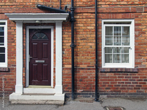 front view of a typical old small english terraced brick house with black painted door and white portico and windows