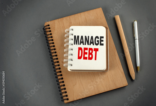 MANAGE DEBT text on notebook with pen and pencil on grey background