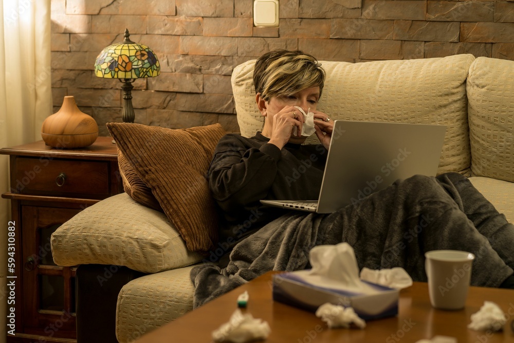 Woman looking at her laptop, while laying on the sofa with high temperature Woman looking at her laptop, while laying on the sofa with high temperature