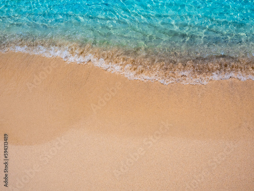 Relaxing beach scene, top view. Movement of blue sea water and wave surf on clean sandy beach ocean, sea shore, coastline, summer vacation holiday background with copy space.