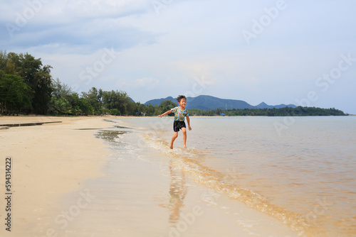 Cheerful Asian boy running on the sand