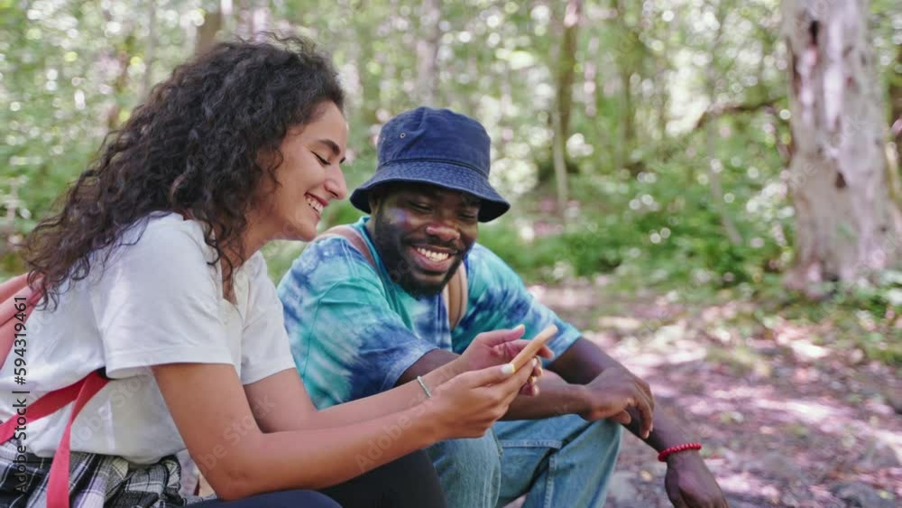 happy couple of black man and arabic woman travelling in forest, sitting on log and viewing photos happy couple of black man and arabic woman travelling in forest, sitting on log and viewing photos