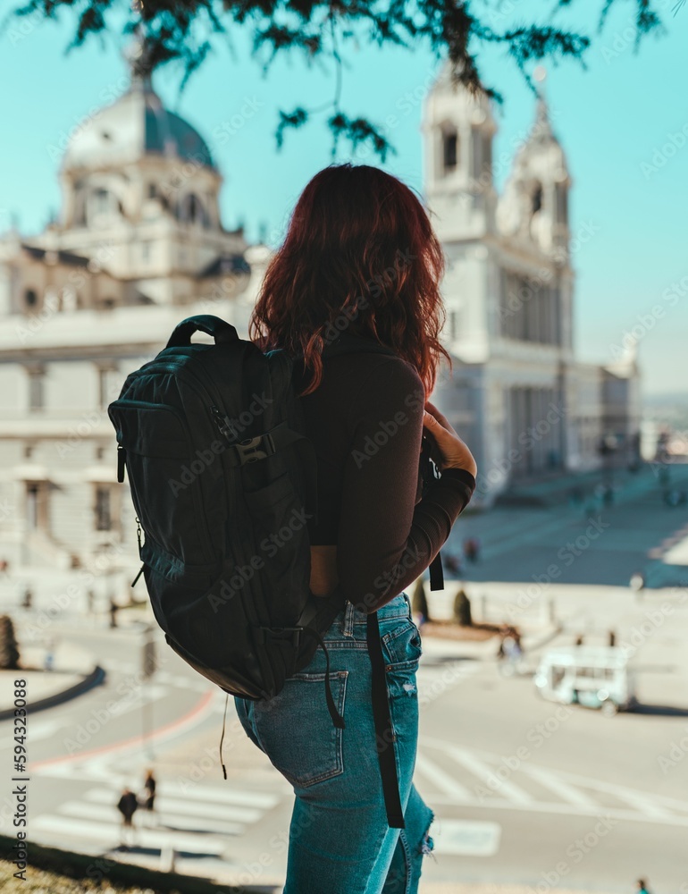 Vertical back view of a young female wearing a black backpack on the street