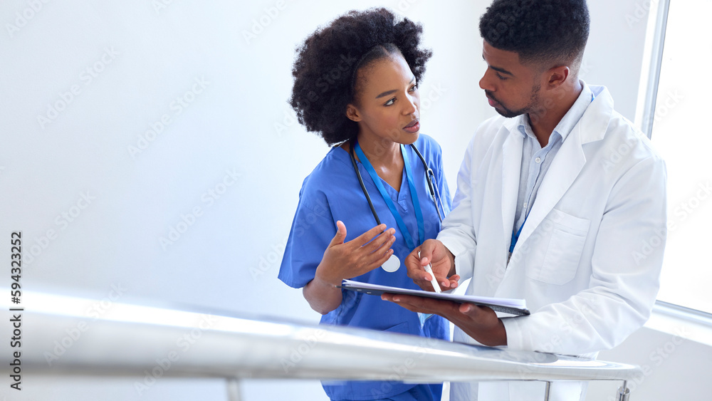 Male Doctor And Female Nurse Discussing Patient Notes On Stairs In Hospital Building Male Doctor And Female Nurse Discussing Patient Notes On Stairs In Hospital Building