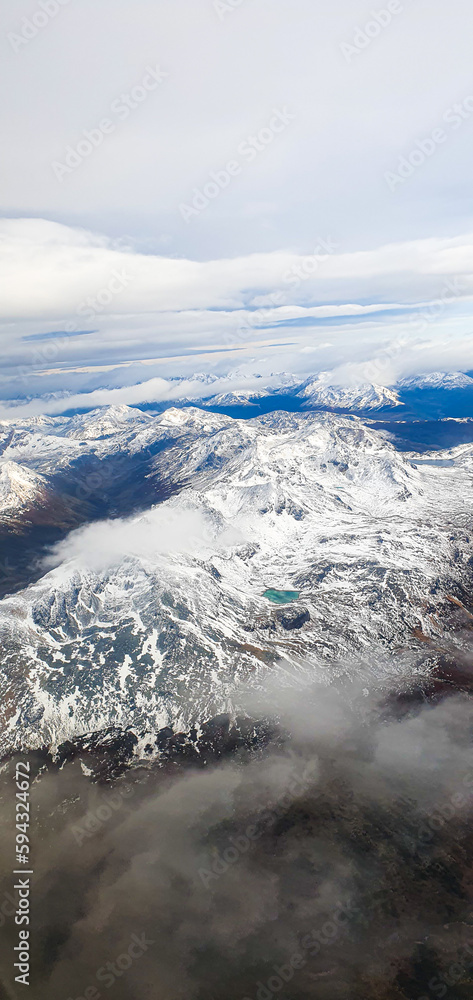 Fototapeta premium Flying over the Andes Mountains with sparse clouds and below the white immensity of snow.