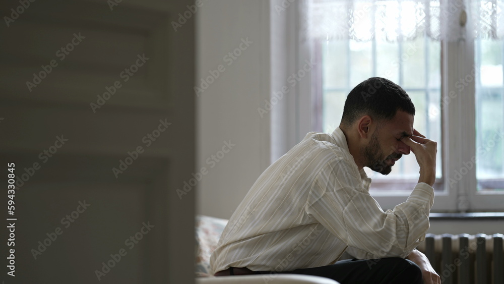 Dramatic moment of One man suffering alone sitting on couch feeling frustration and desperation during difficult times Dramatic moment of One man suffering alone sitting on couch feeling frustration and desperation during difficult times