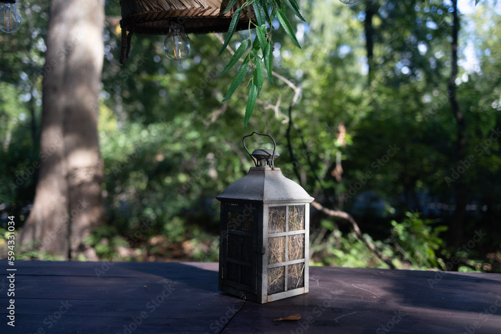 A beautiful decoration in the form of a large lantern and candlestick stands on a table illuminated by the morning sun on a wonderful summer day.morning. The concept of aesthetic relaxation in nature.