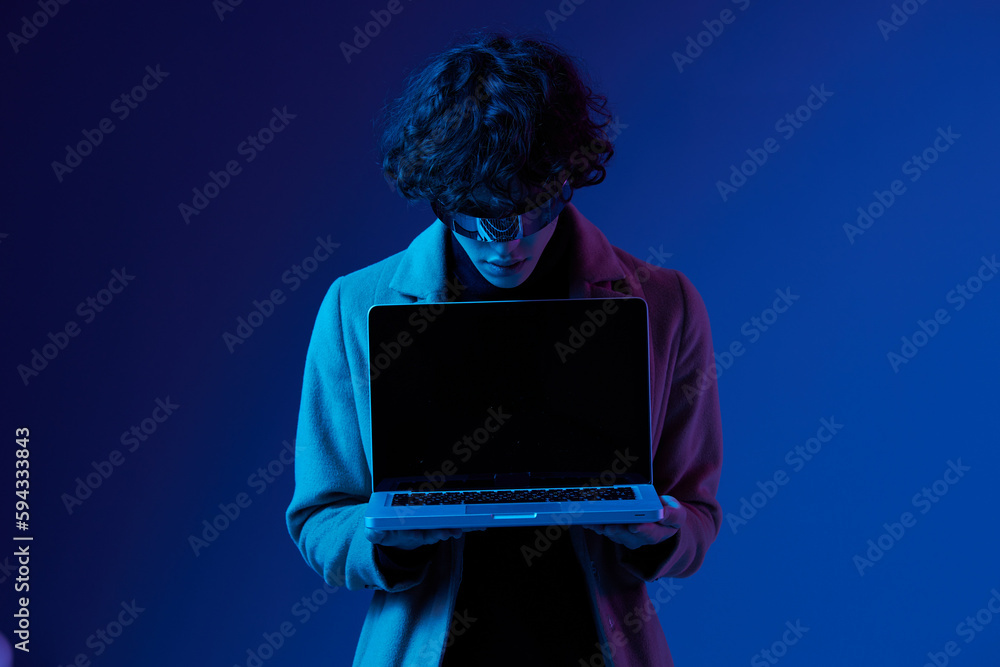 Portrait of a stylish male hacker with a laptop and futuristic glasses in blue light, Blue Perennial color, cyber security, technology, open laptop copy space, template Portrait of a stylish male hacker with a laptop and futuristic glasses in blue light, Blue Perennial color, cyber security, technology, open laptop copy space, template