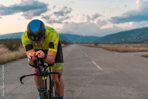  Triathlete riding his bicycle during sunset, preparing for a marathon. The warm colors of the sky provide a beautiful backdrop for his determined and focused effort.