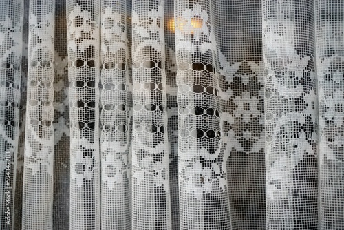 Altmodische weiße transparente Gardinen mit Blumenmuster hinter Glasscheibe von Fenster mit goldgelbem Licht © Anette