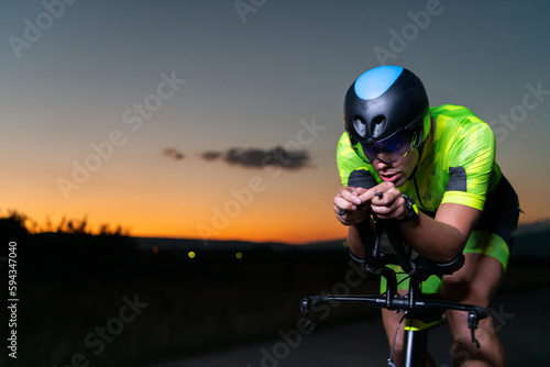 Fototapeta Naklejka Na Ścianę i Meble -  A triathlete rides his bike in the darkness of night, pushing himself to prepare for a marathon. The contrast between the darkness and the light of his bike creates a sense of drama and highlights the