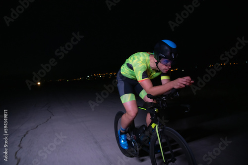 A triathlete rides his bike in the darkness of night, pushing himself to prepare for a marathon. The contrast between the darkness and the light of his bike creates a sense of drama and highlights the