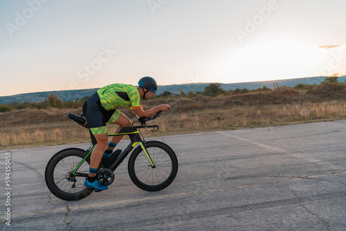  Triathlete riding his bicycle during sunset, preparing for a marathon. The warm colors of the sky provide a beautiful backdrop for his determined and focused effort.