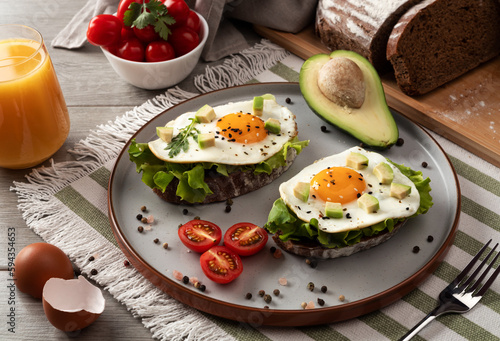 Toasts with avocado and fried eggs on table. Healthy breakfast with vegetables and herbs. Fried egg on a grey plate with orange juice. Serving on the table. 