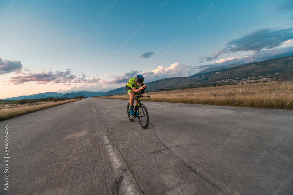 Triathlete riding his bicycle during sunset, preparing for a marathon. The warm colors of the sky provide a beautiful backdrop for his determined and focused effort. Triathlete riding his bicycle during sunset, preparing for a marathon. The warm colors of the sky provide a beautiful backdrop for his determined and focused effort.