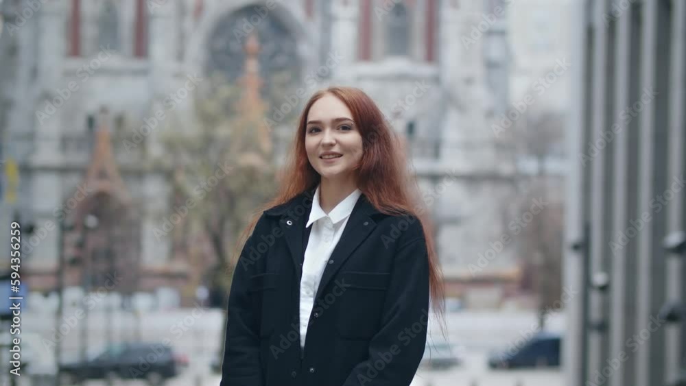 Happy girl in black coat posing on city background with smile. Stylish ginger woman smiles to camera Happy girl in black coat posing on city background with smile. Stylish ginger woman smiles to camera