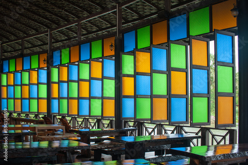 Colorful Window in the class room with many table and chair.